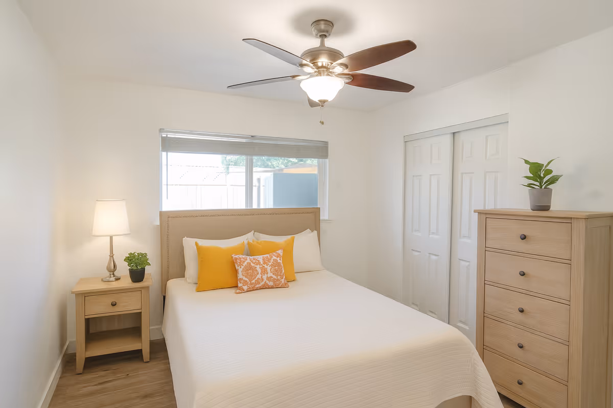 Bright bedroom with bed, nightstand, dresser, ceiling fan, and simple decor.