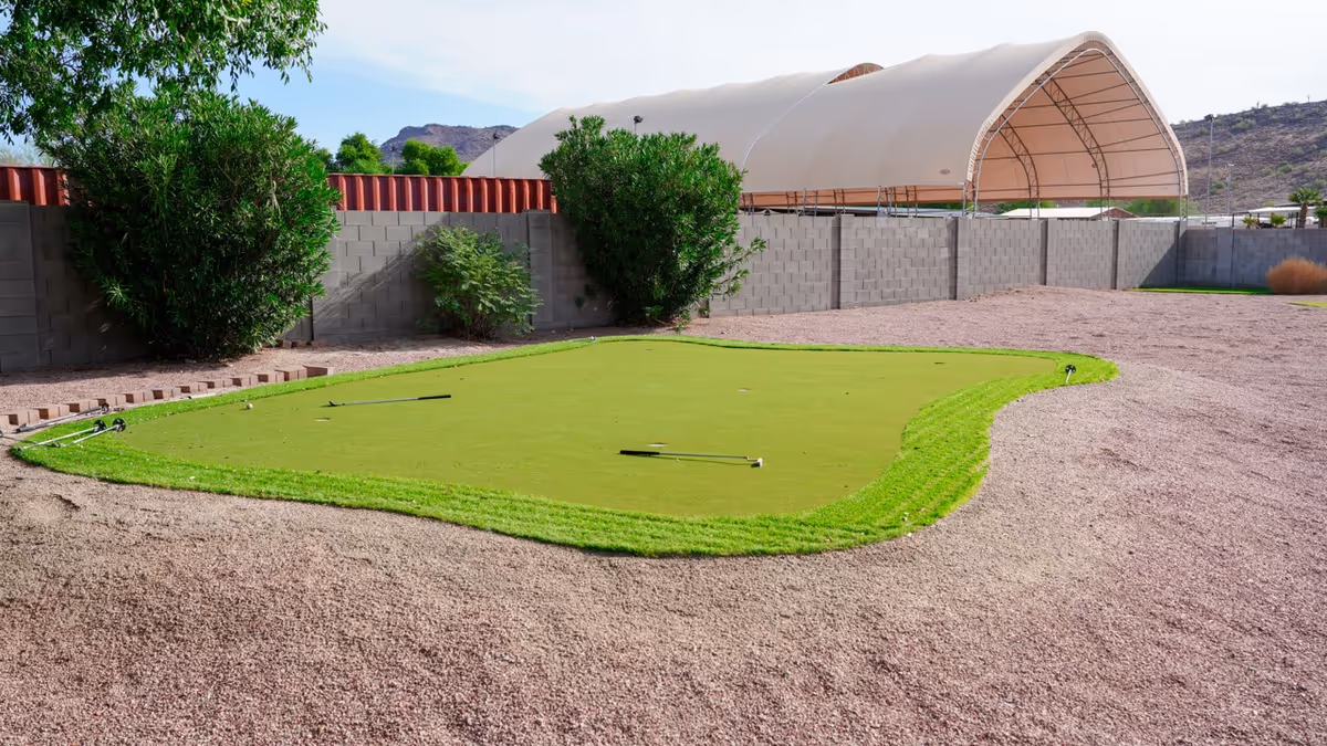 Outdoor facility yard with a small putting green, gravel surface, and a large canopy.