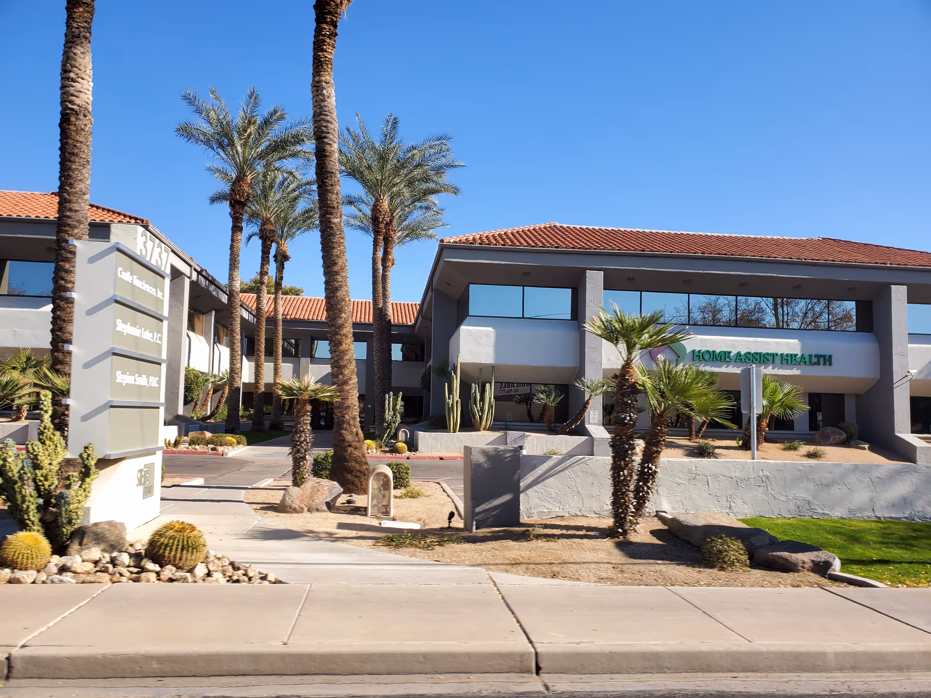 Exterior view of a modern senior living facility with palm trees and a sign.