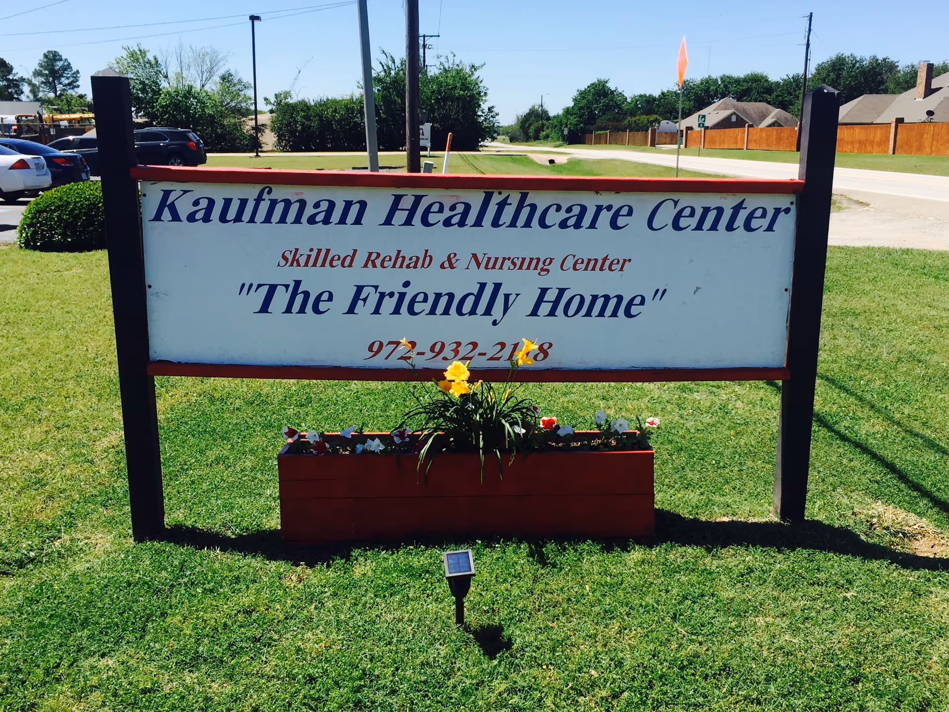 Outdoor sign on a grassy lawn reading "Kaufman Healthcare Center - 'The Friendly Home'".
