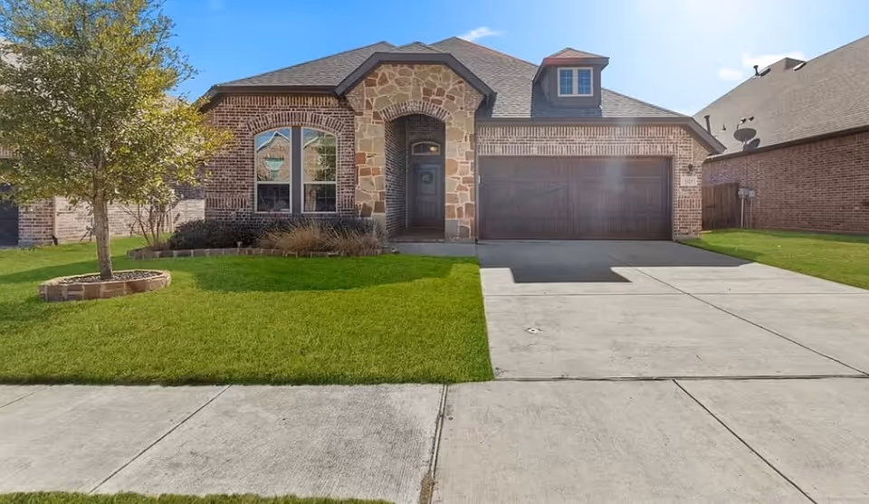 Brick and stone suburban home with a two-car garage, green lawn, and driveway.