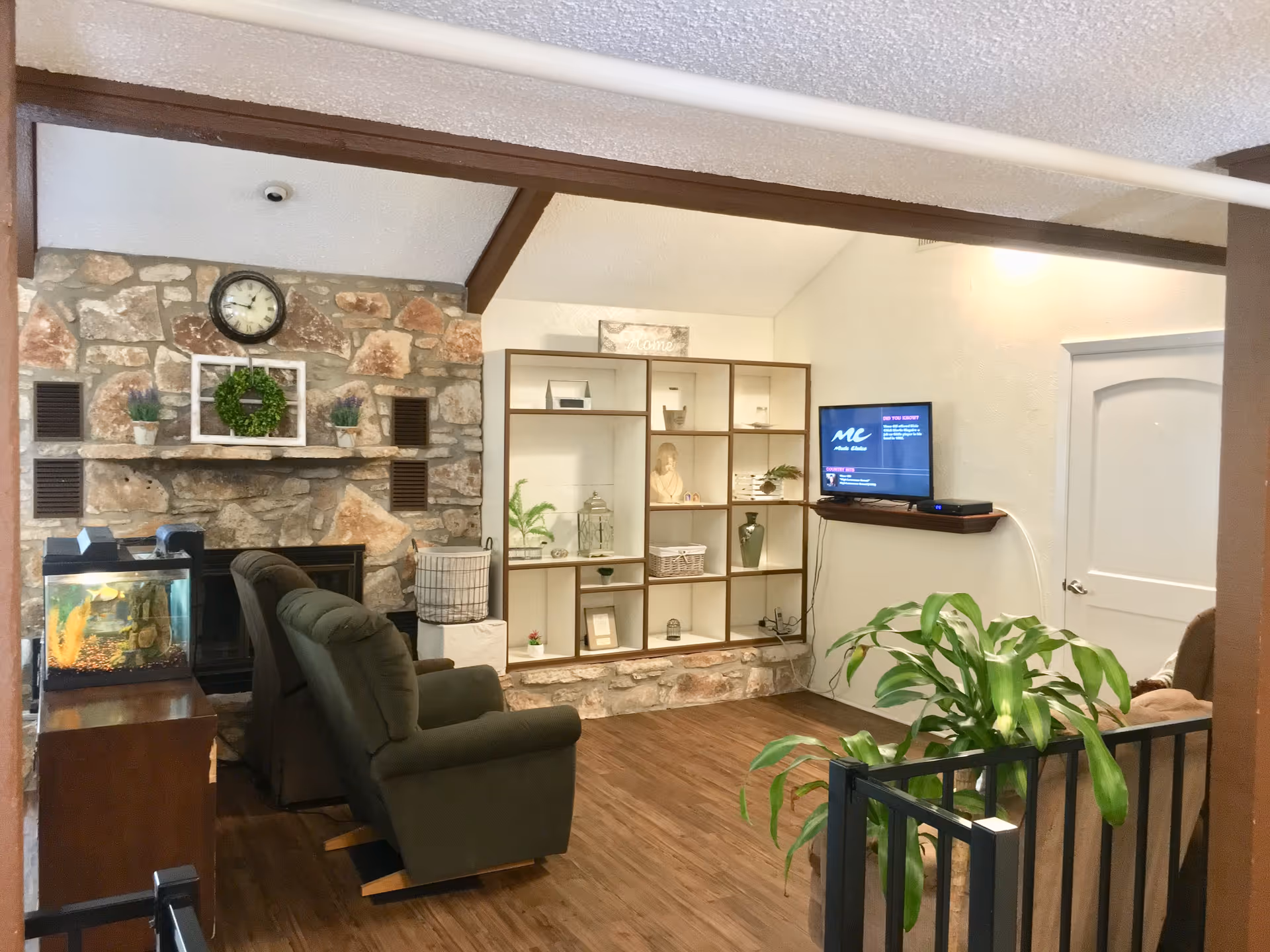 Cozy living room in a senior facility featuring a stone fireplace, shelves, and TV.
