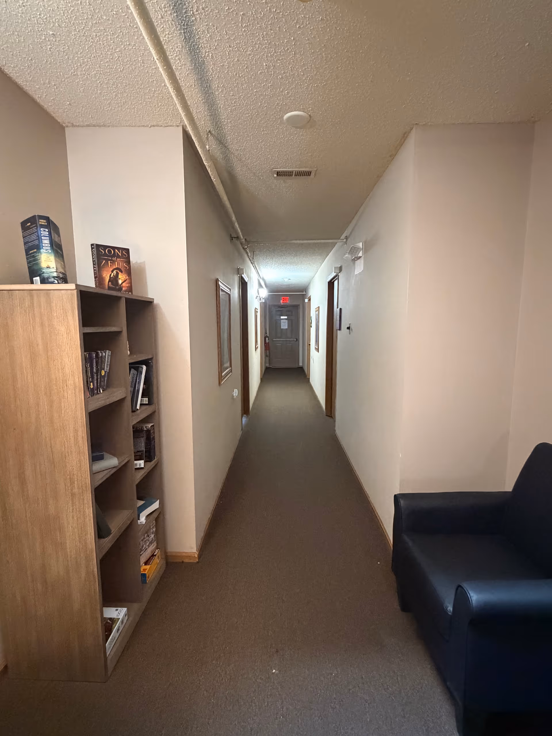 A long interior hallway in a senior living facility with a bookshelf and a blue chair.