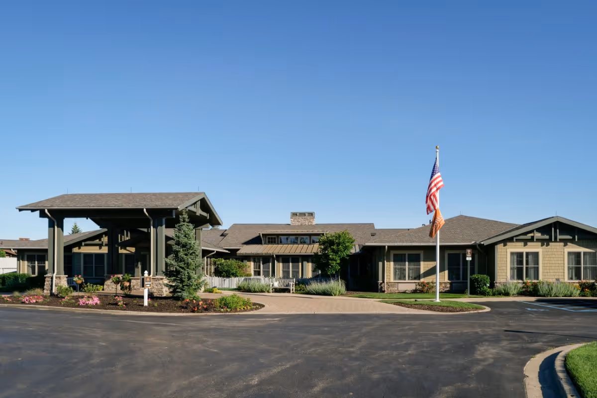 Front exterior of the Sunrise of Cascade facility with a covered entrance, flagpole, and landscaping under a clear blue sky.