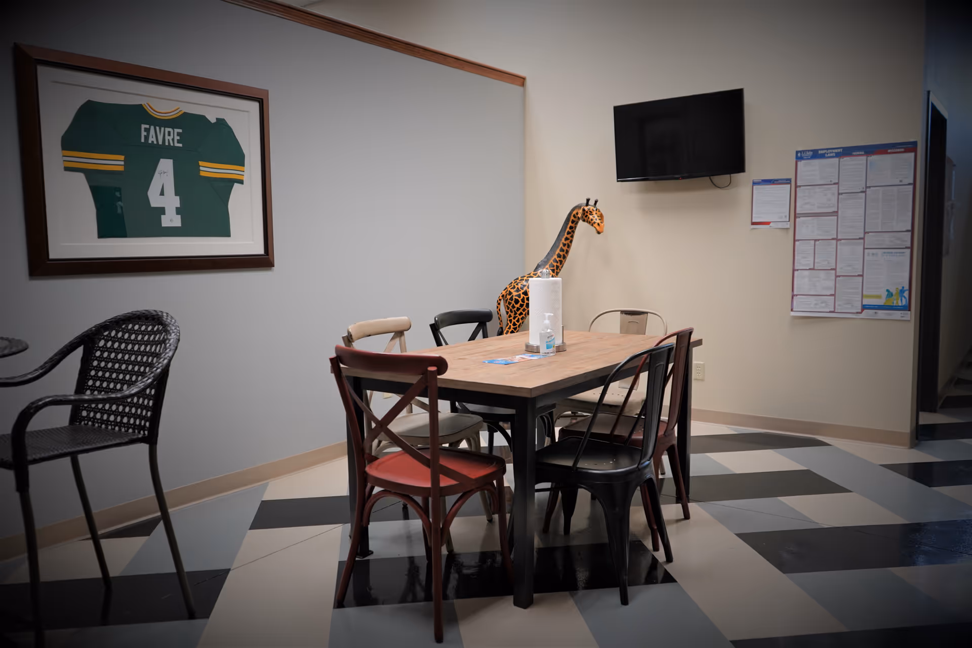 Interior dining area with a wooden table, colorful chairs, giraffe decor, and wall-mounted TV.
