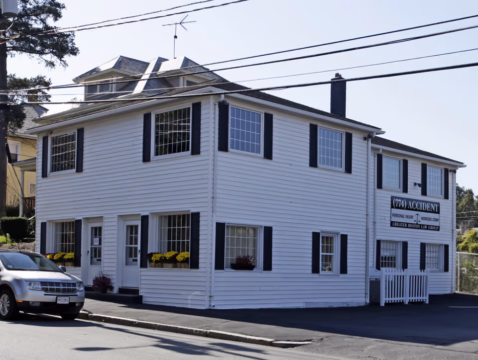 White two-story building with black shutters along a street; no people visible.