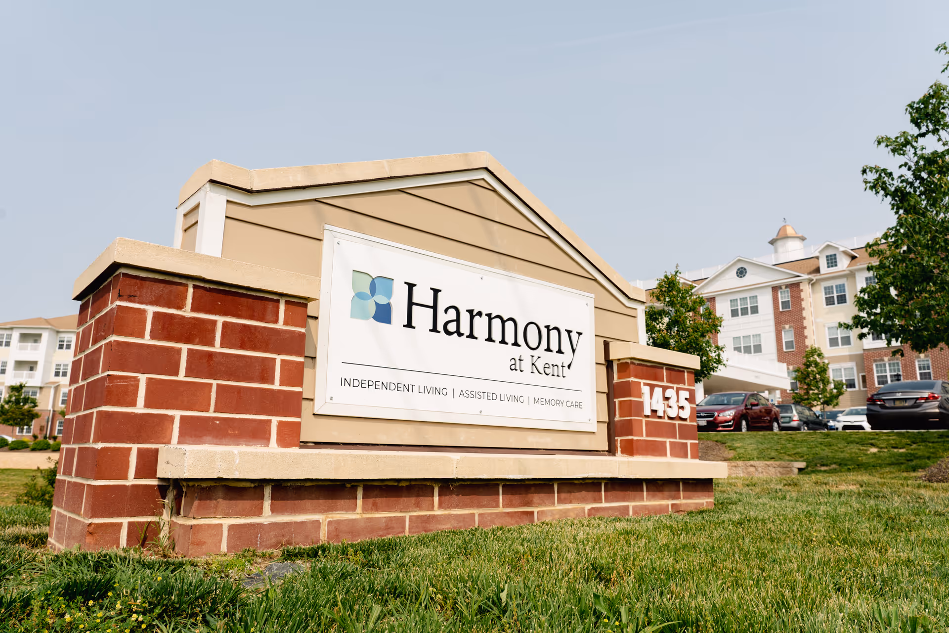 Front view of Harmony at Kent sign with brick base and adjacent building.