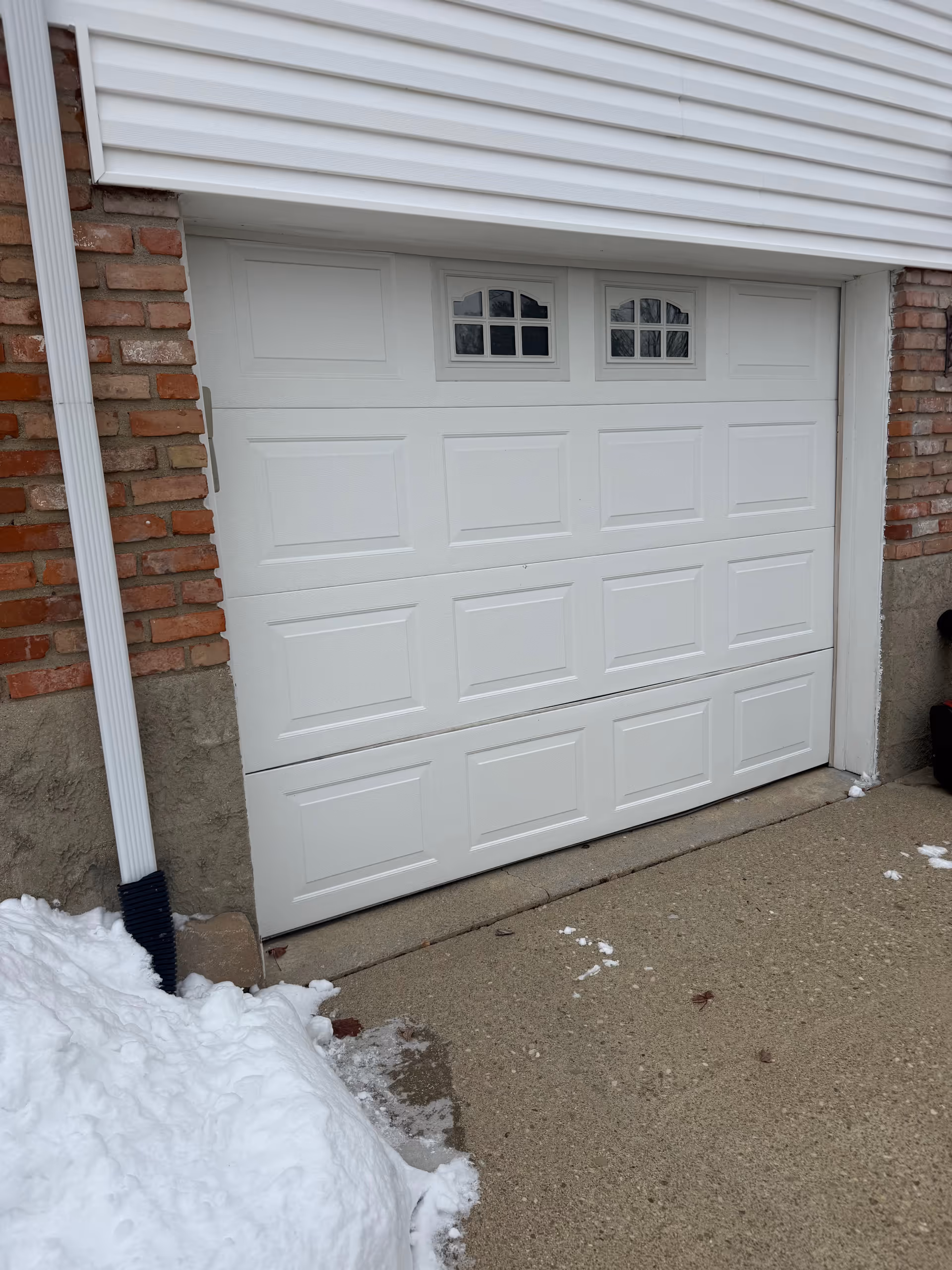White garage door on brick house exterior with downspout and snow nearby