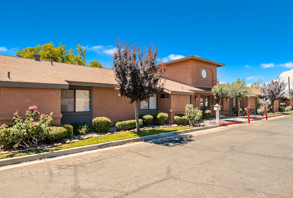 Exterior view of Valley Crest Memory Care facility with stucco walls, landscaping, and blue sky.