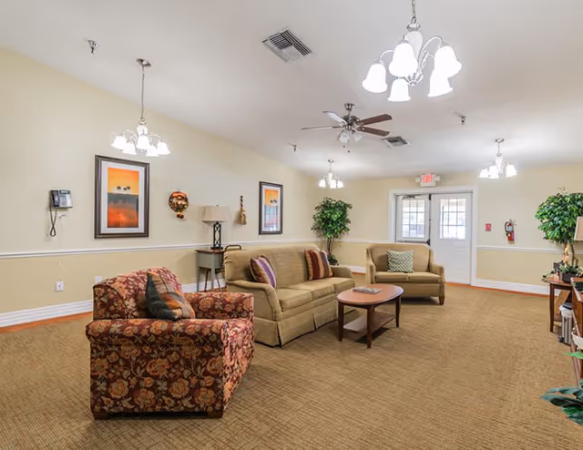 Spacious senior living common room with beige sofas, chairs, coffee table, and wall art.