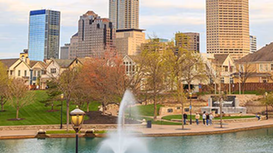 City park featuring a fountain, trees, and a skyline of tall buildings.