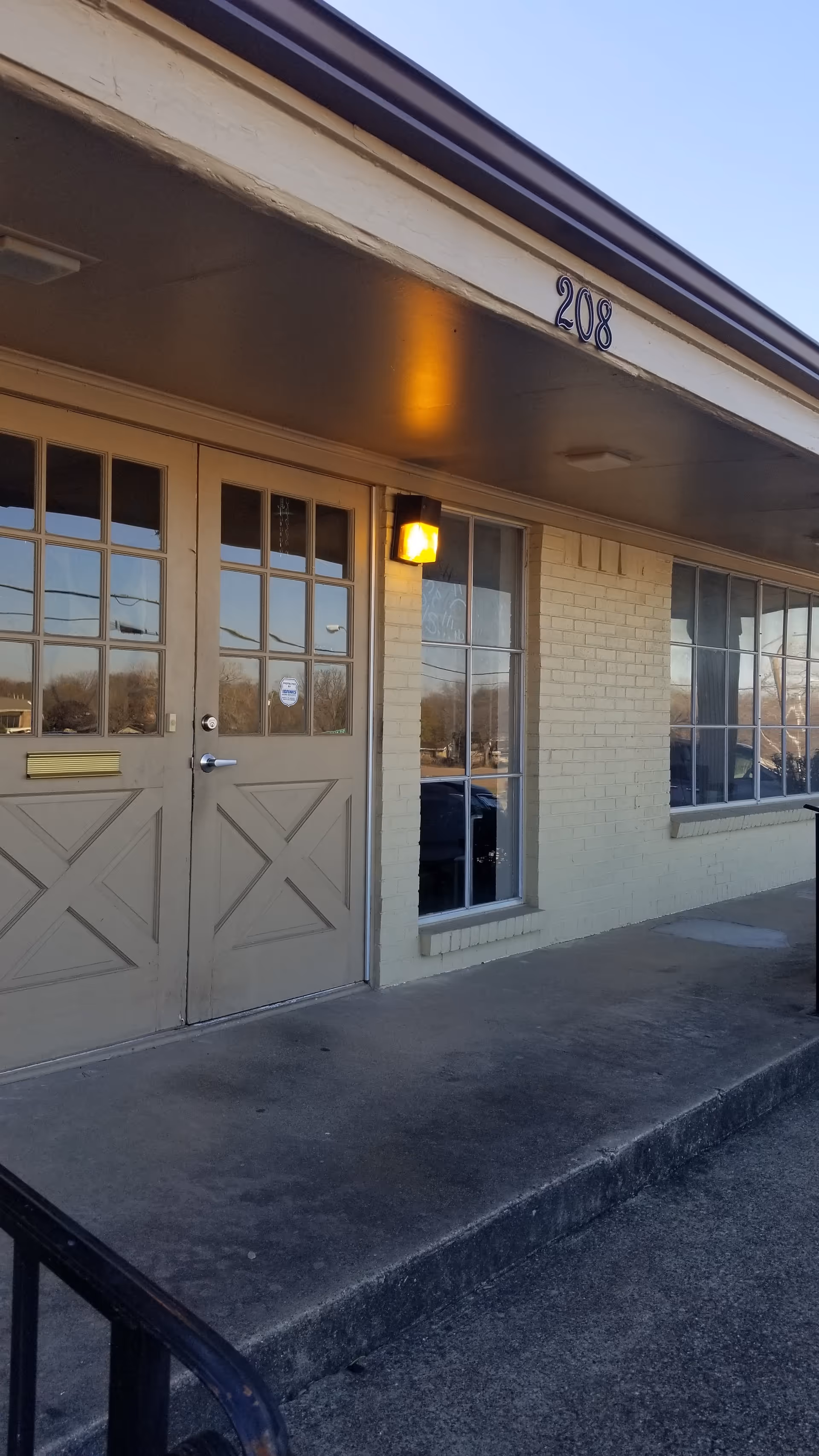 Exterior view of a facility entrance with double doors, windows, and the number 208.