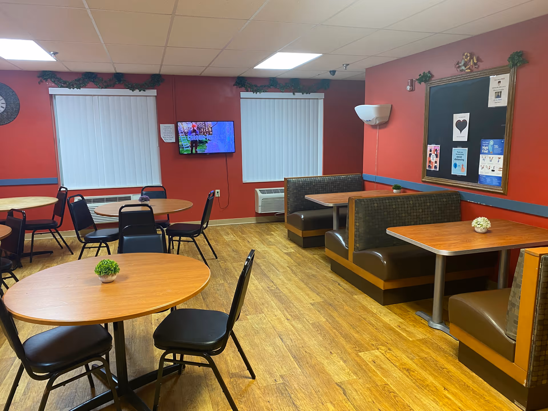 Painted red dining area with round tables, booths, chairs, and wall-mounted TV.
