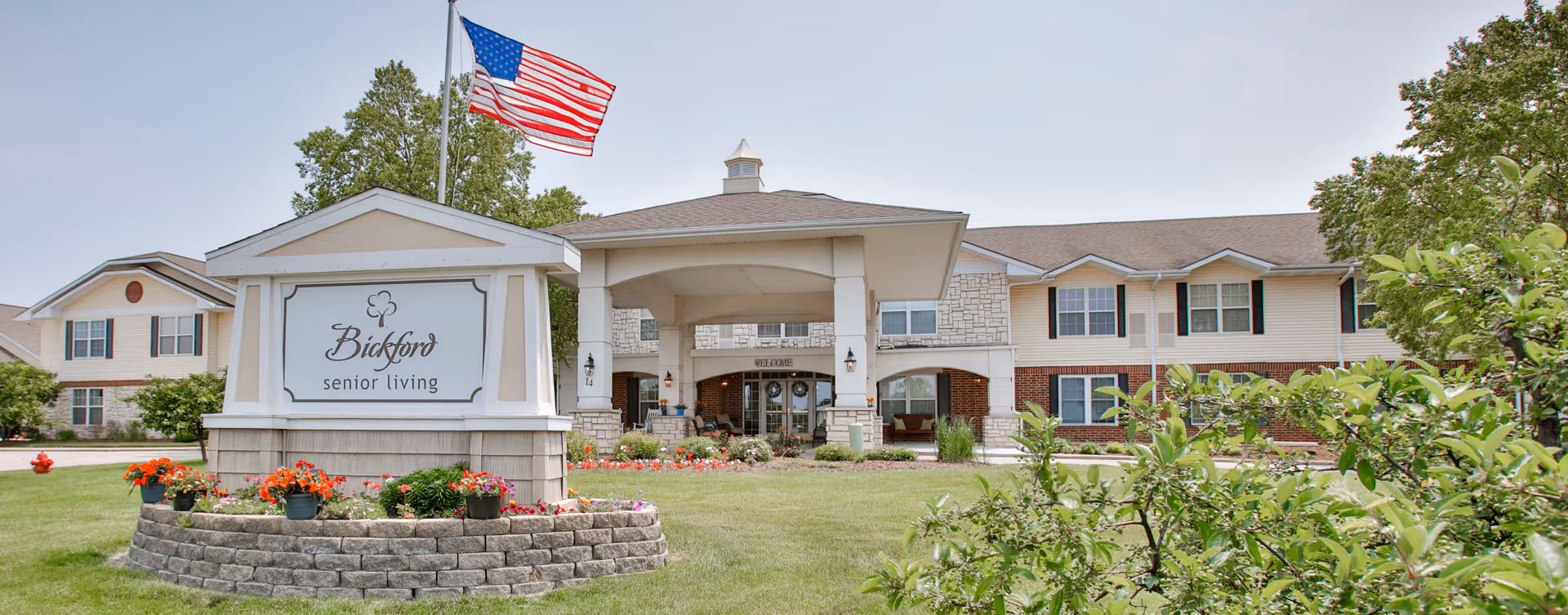 Exterior view of Bickford of Bloomington senior living with flag and landscaped entrance.