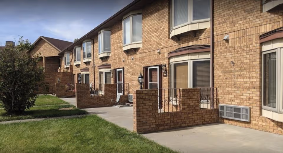 Brick exterior of a multi-unit senior living building with small patios, bay windows, and a grassy lawn.