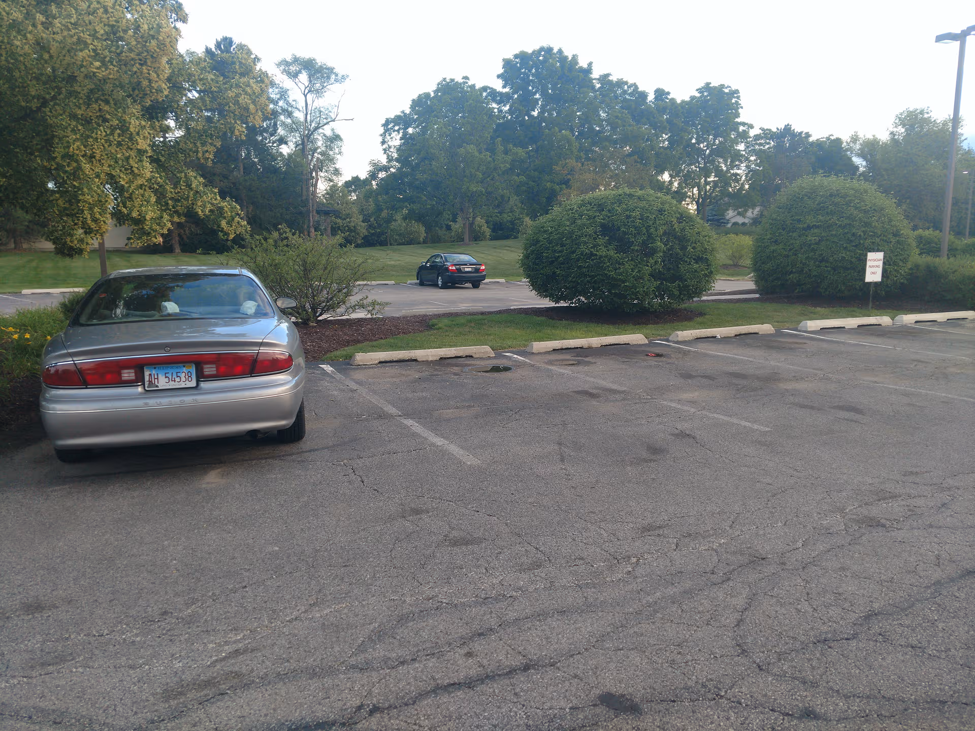 Exterior parking lot at Alden Estates of Barrington with a silver car and landscaped greenery.