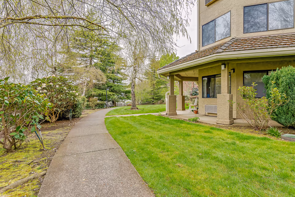 Curved sidewalk leads to a tan Solstice Senior Living at Bellingham building with a grassy lawn.