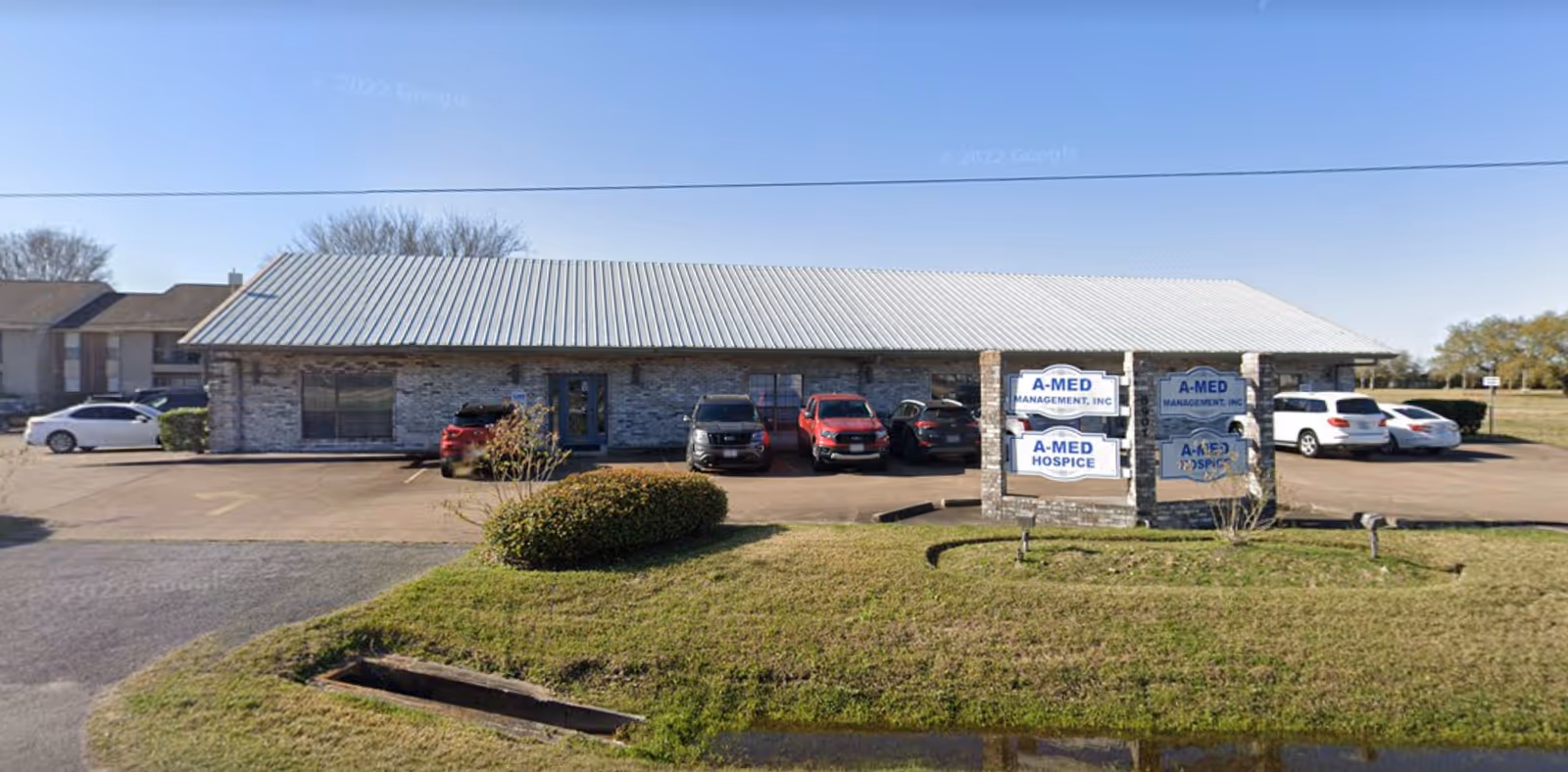 Single-story stone building with metal roof, parking lot, and A-MED Hospice sign.