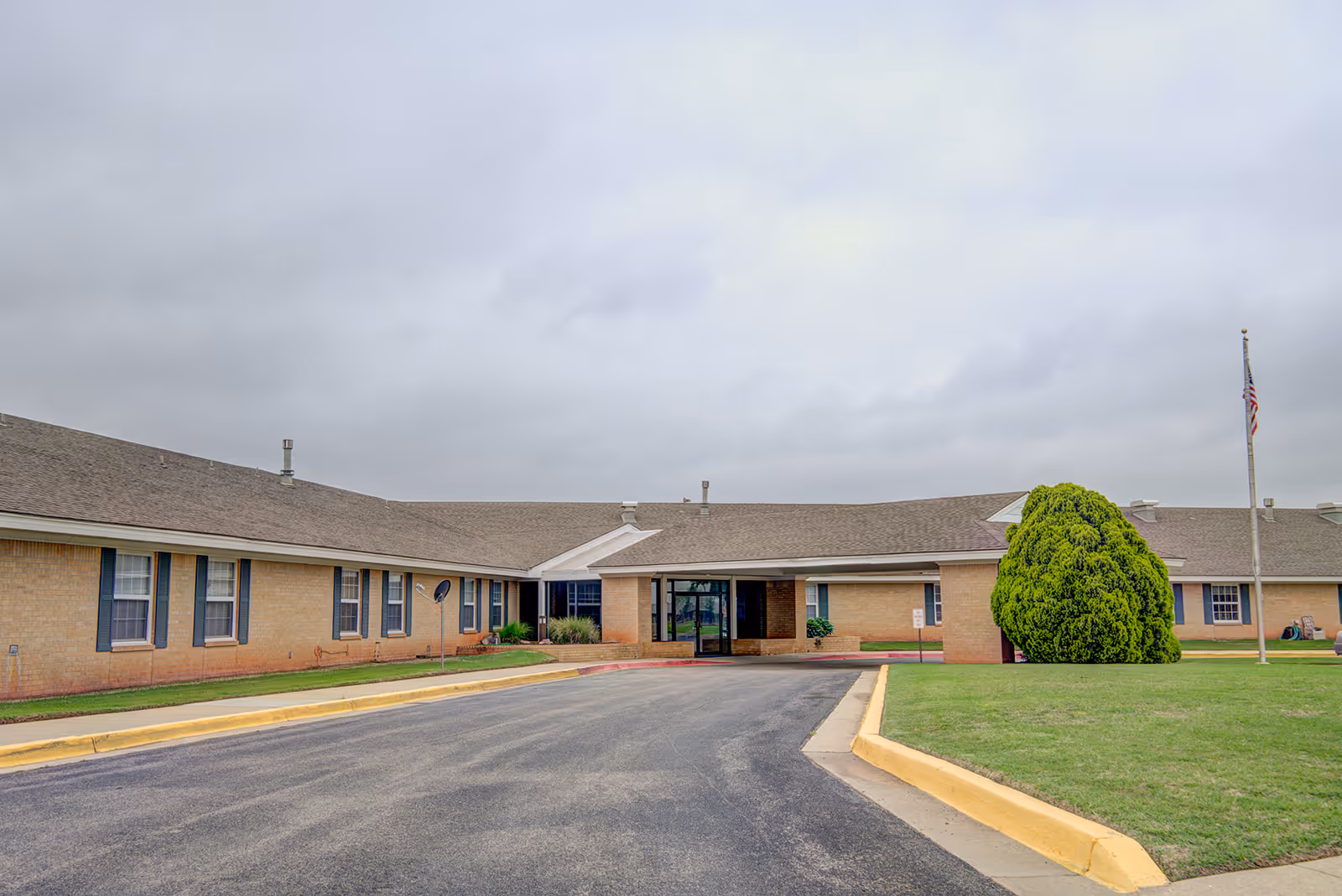 Single-story brick assisted living facility exterior with front entrance, driveway, and manicured lawn.