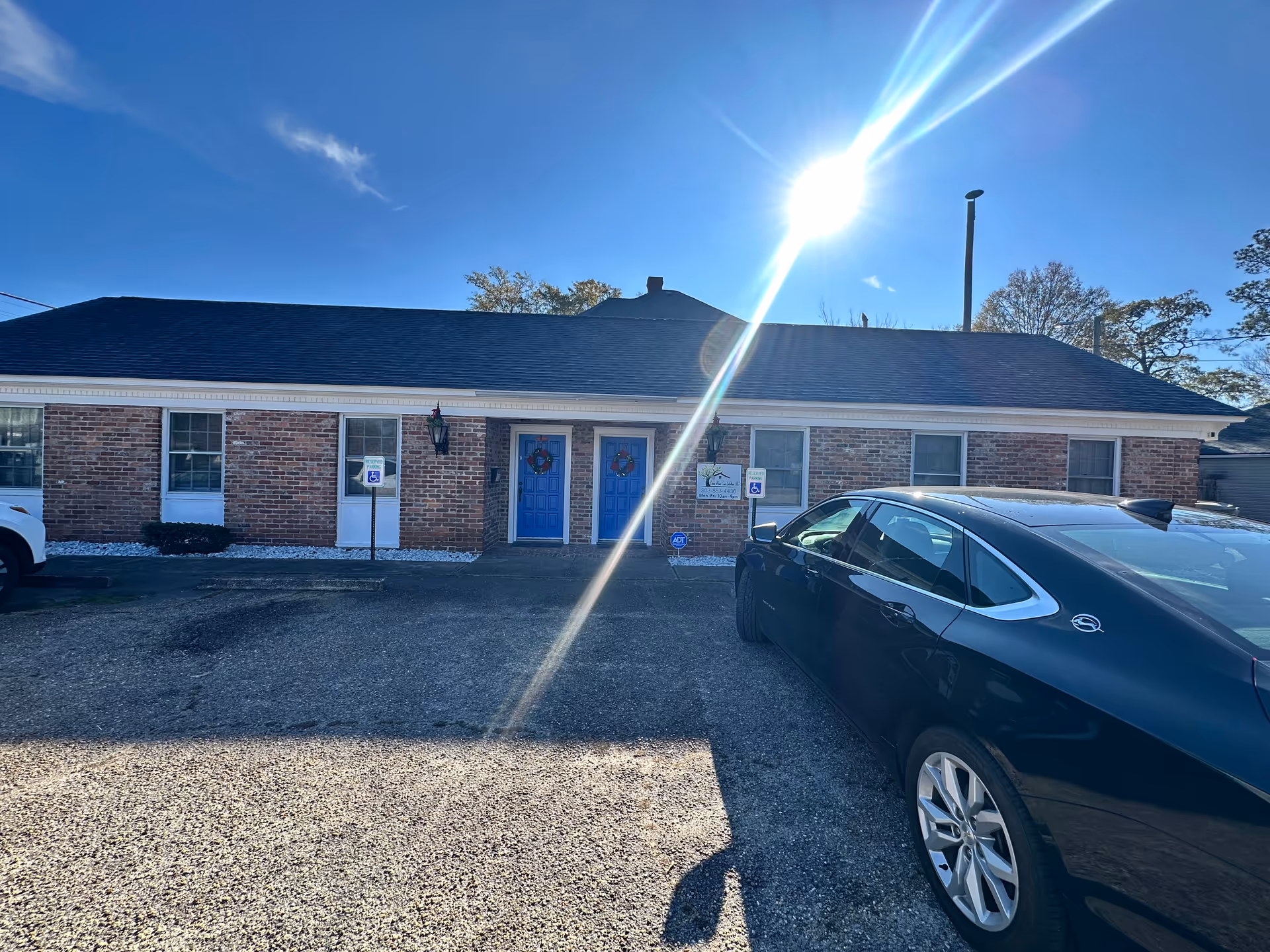Brick facility exterior with blue doors, parked cars, and bright sun glare.