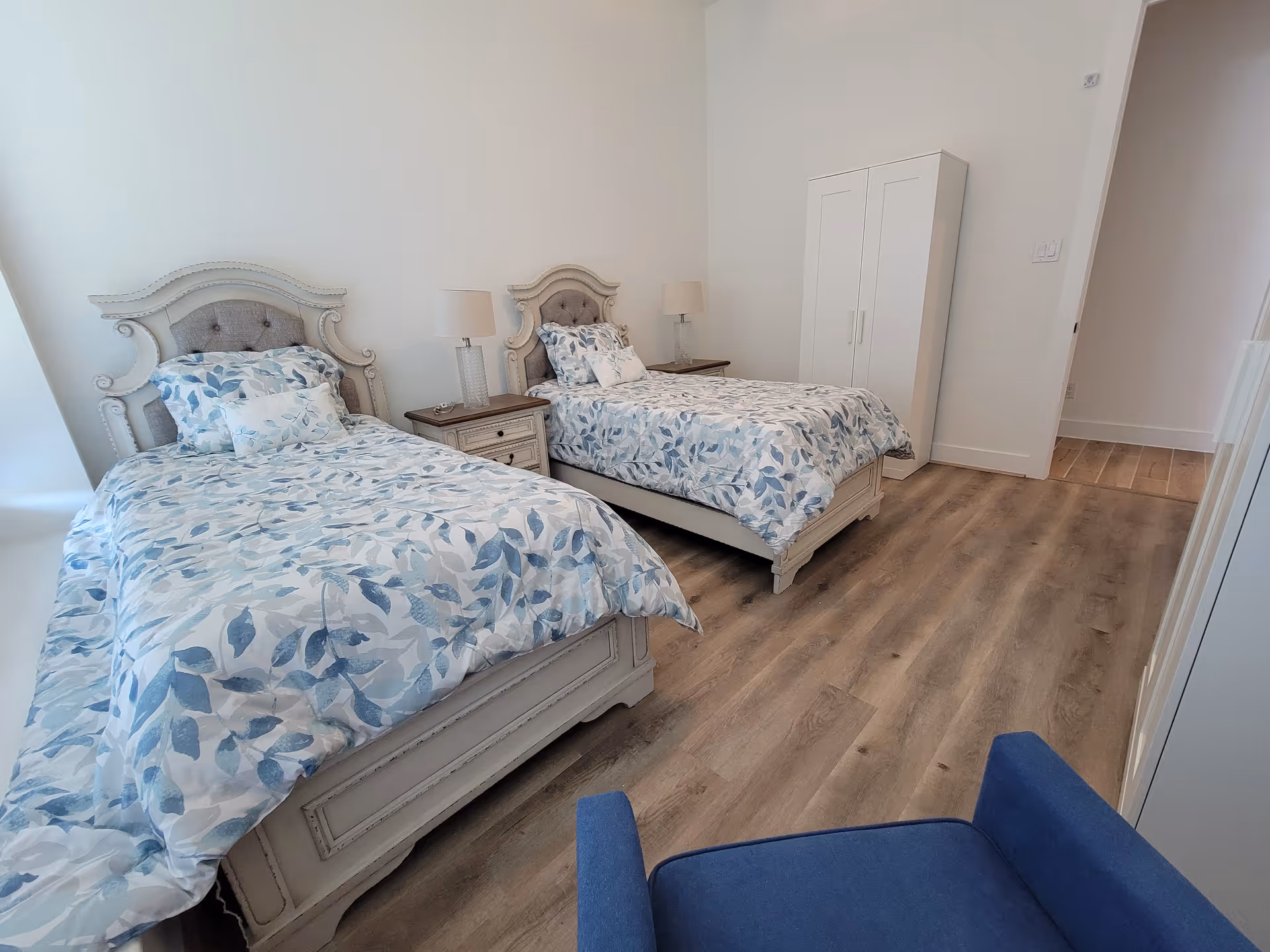 Two twin beds with blue leaf-patterned bedding in a bright bedroom.