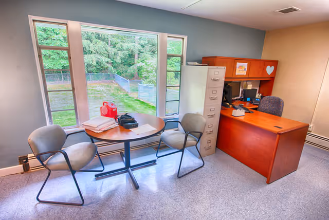 Office area with a round table, three chairs, filing cabinet, and a desk by windows.