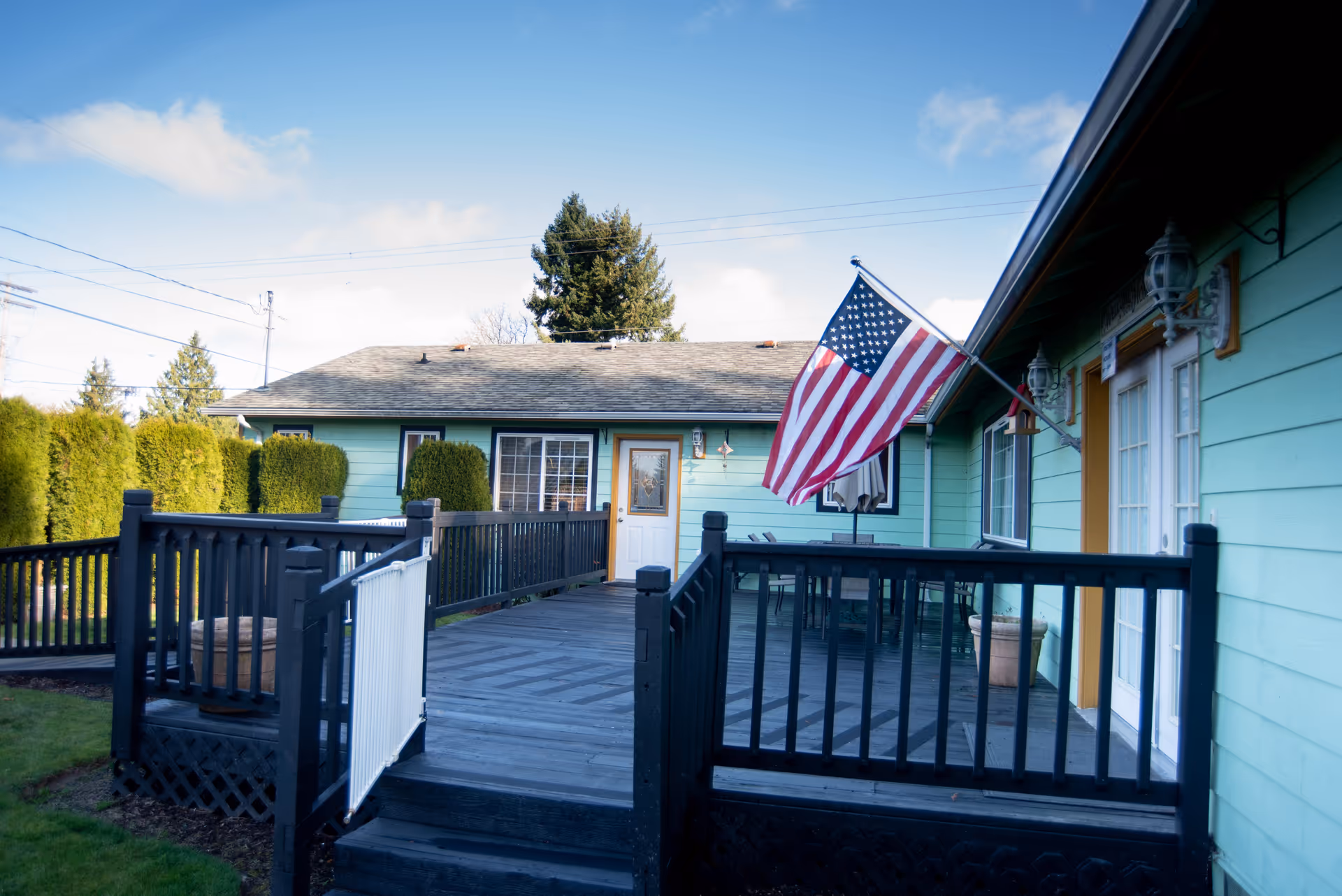 A teal single-story building with a wooden deck, railing, and waving American flag.