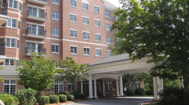 Brick multi-story building with a covered porte-cochere entrance, landscaping, and trees.