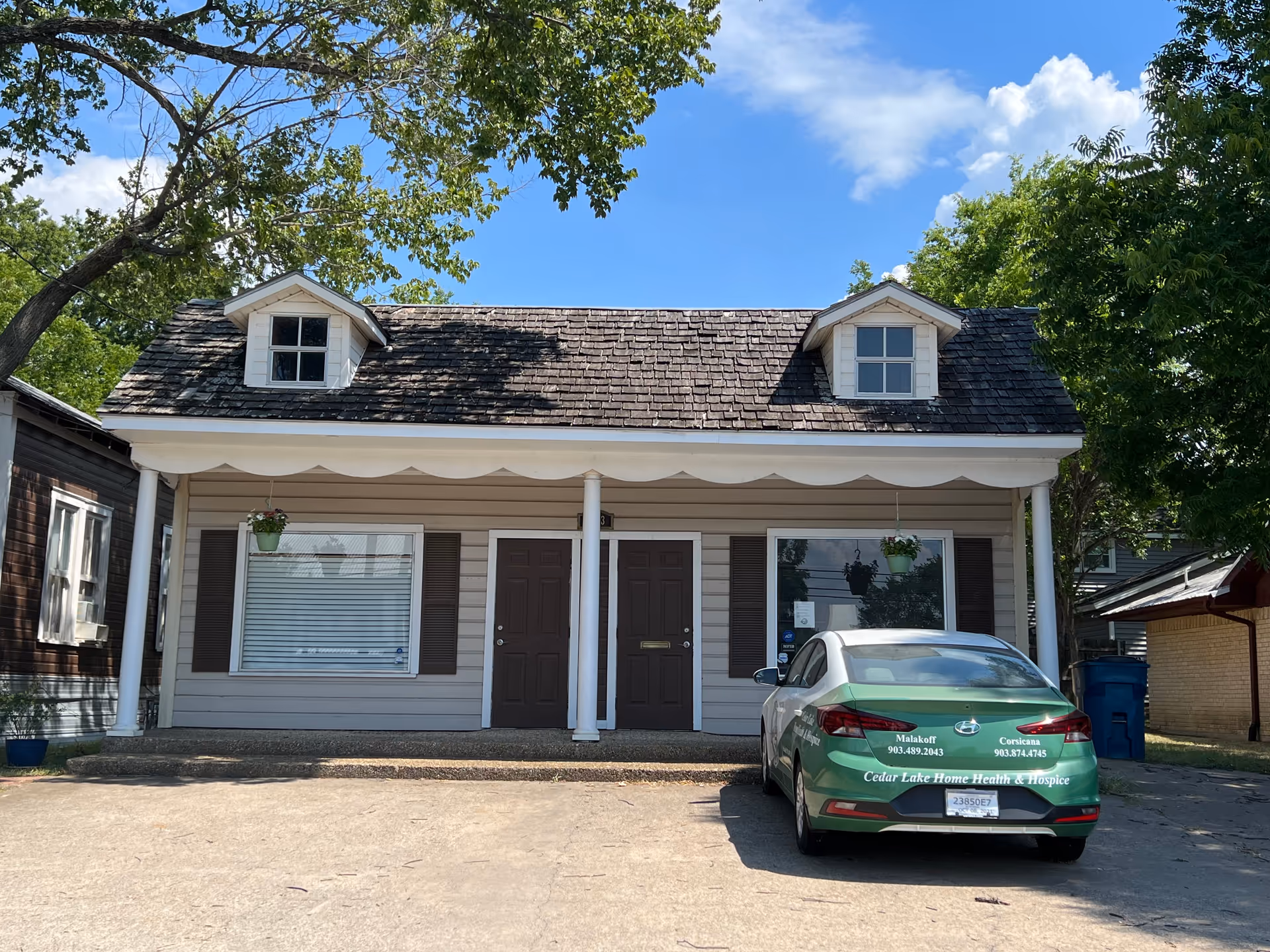 Small beige building with dormers, a front porch, and a green Cedar Lake car parked outside.