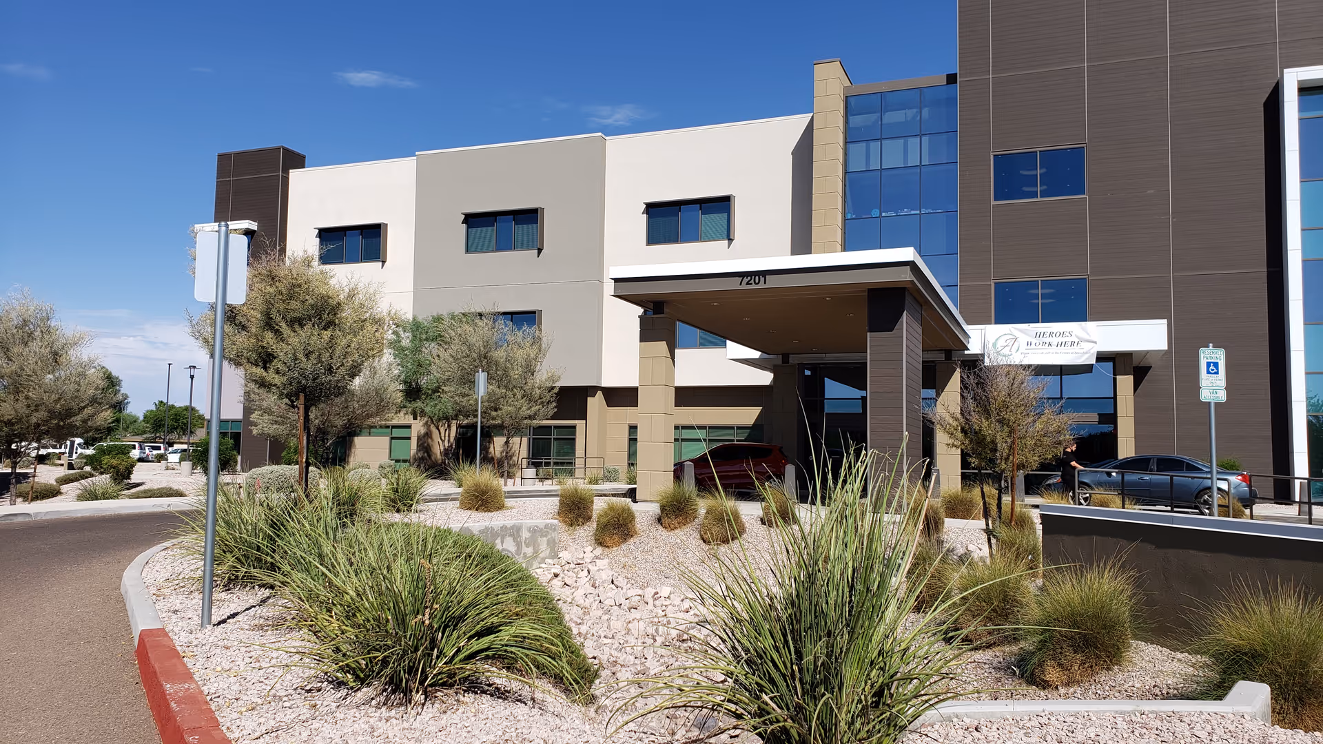 Modern senior living center front with a covered entrance and desert landscaping.