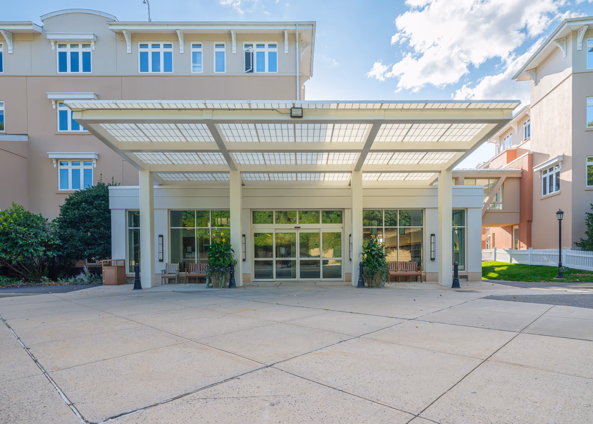 Covered main entrance and drop-off canopy of a multi-story senior living building with benches and planters.