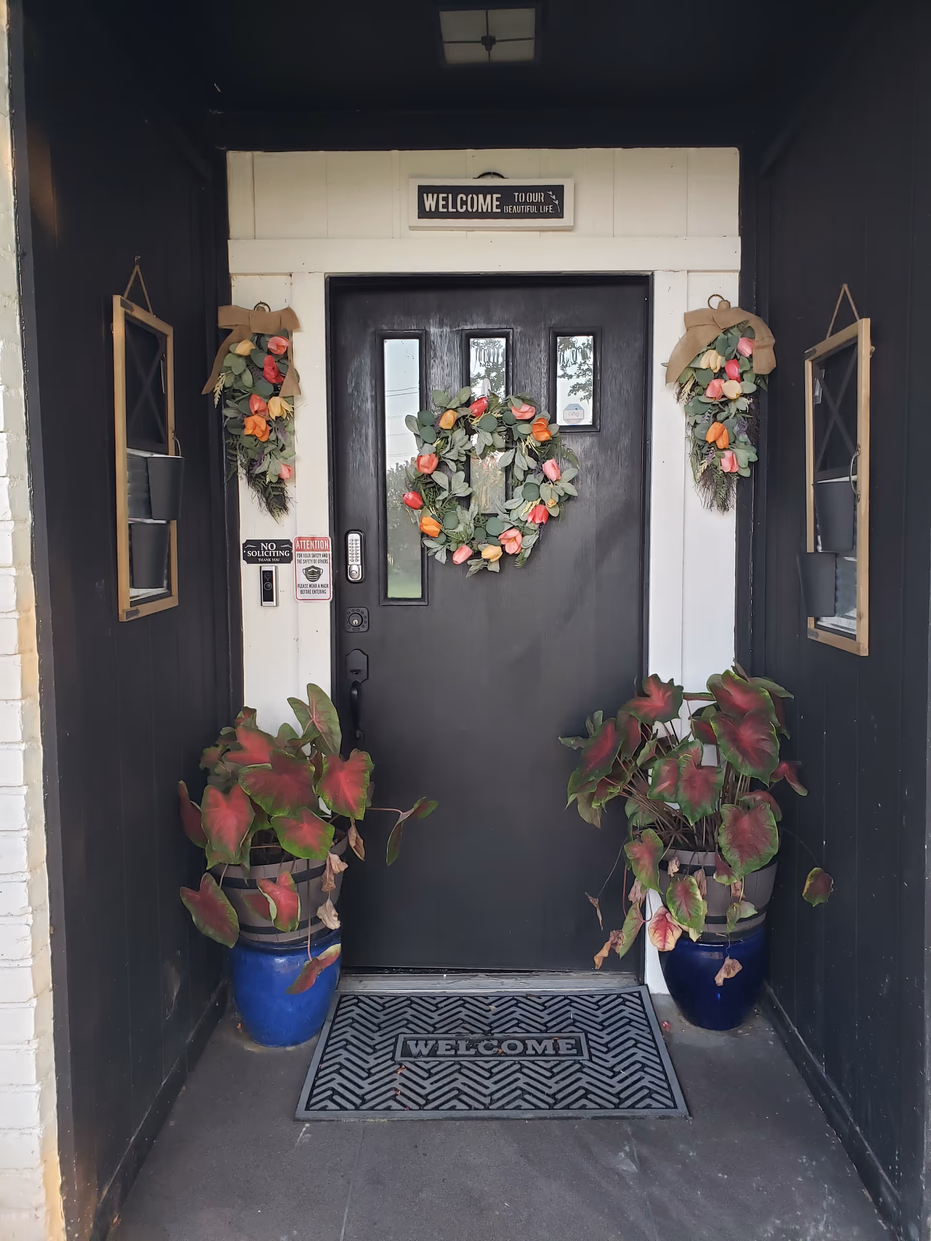 Black front door with decorative wreaths and potted plants at entrance.