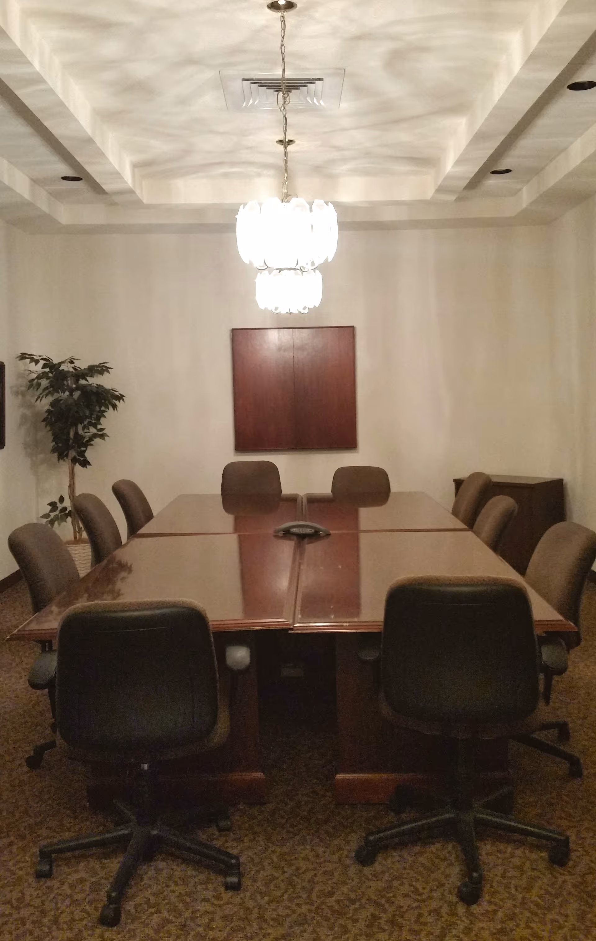 A long wooden conference table with rolling chairs in a bright, formal meeting room.