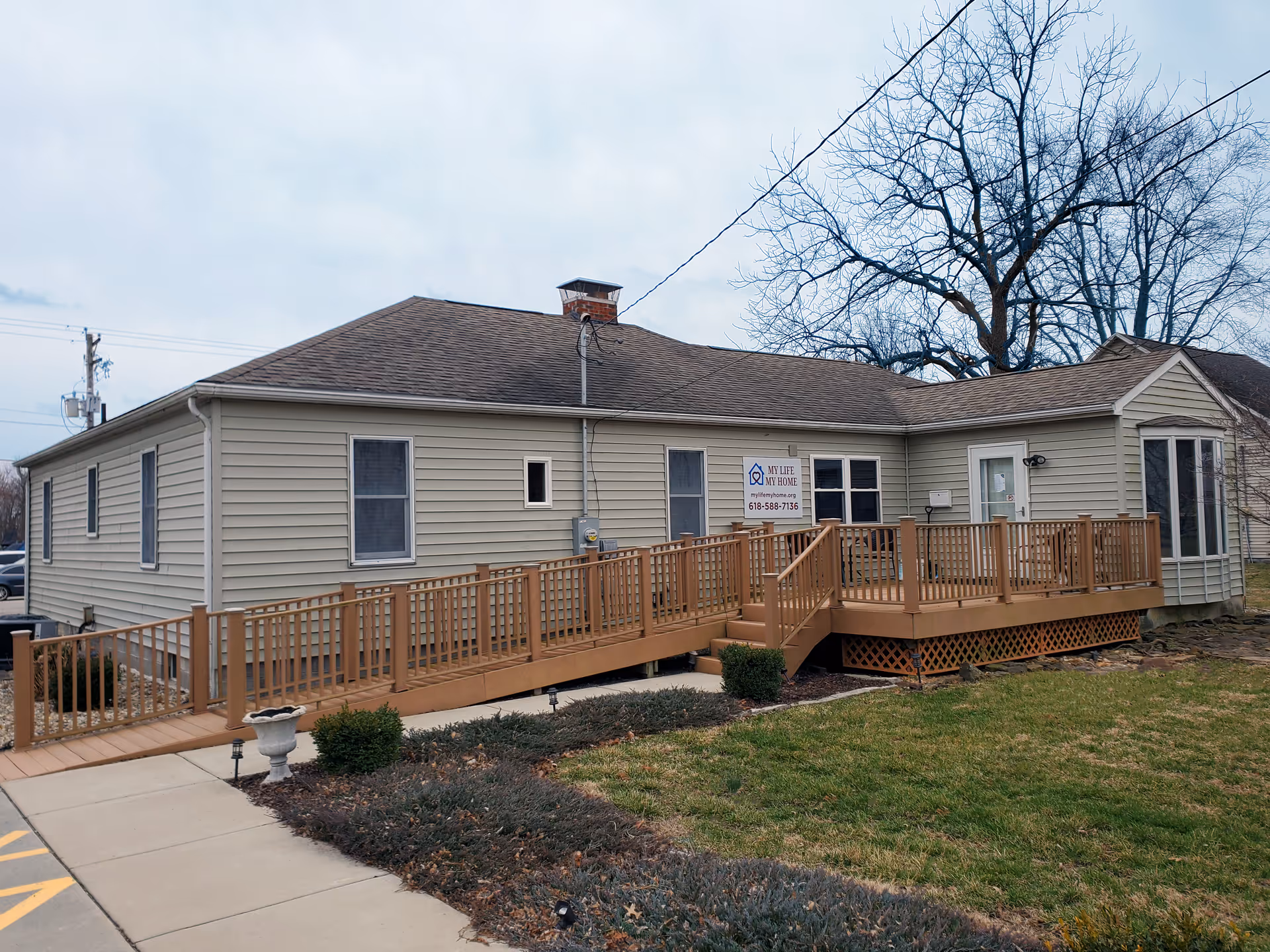Single story beige senior facility with a long wooden ramp to the front entrance.