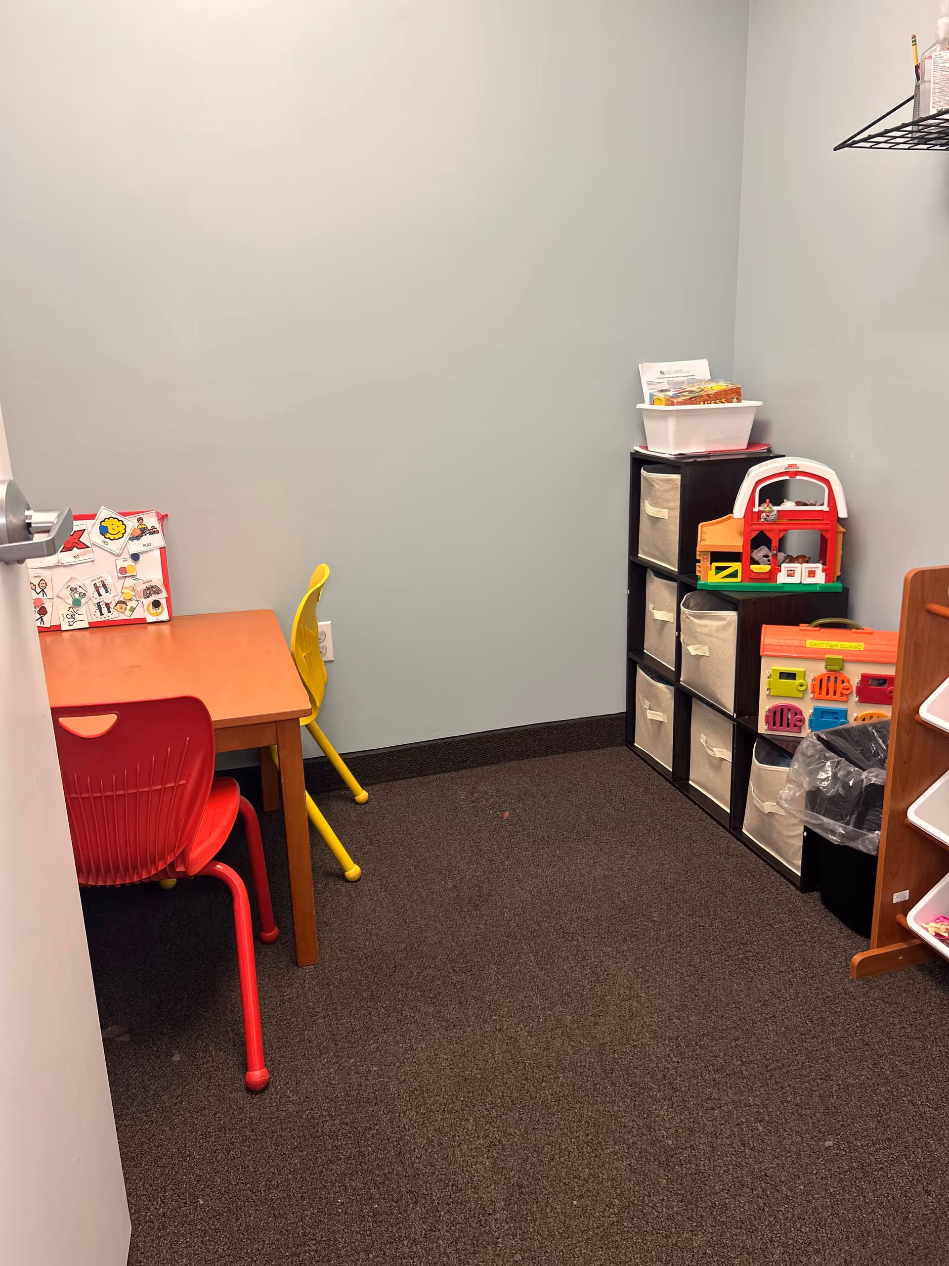 Small sensory play area with colorful chairs, a table, and toy storage against light blue walls.
