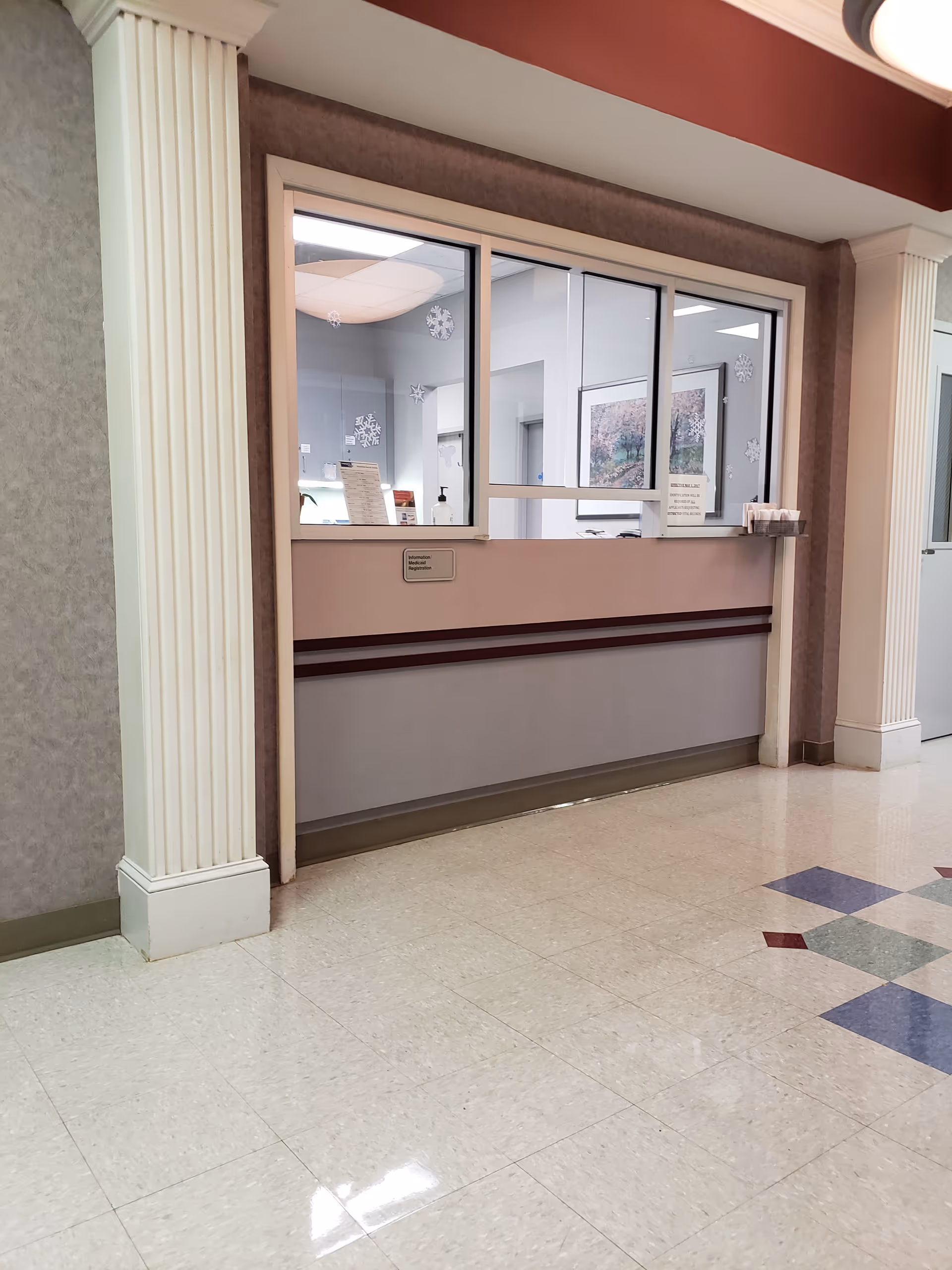 Interior hallway at a senior facility with a front desk window and decorative columns.