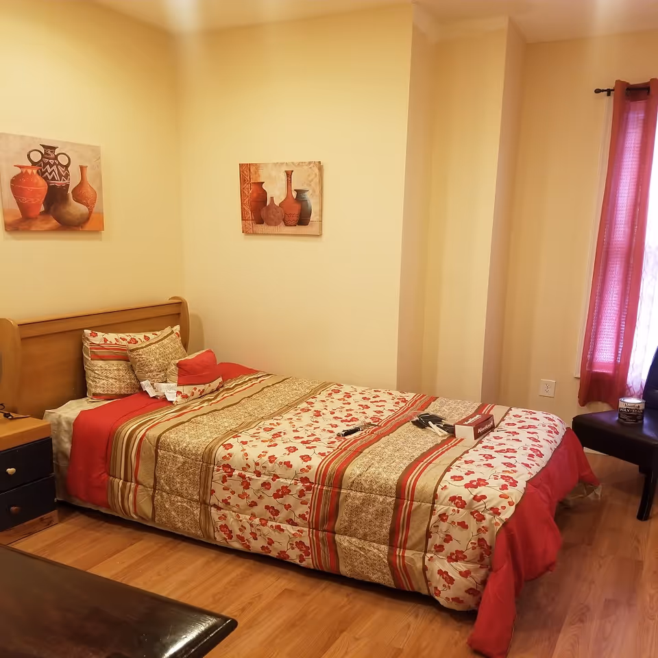 Bedroom with a wooden bed, floral quilt, pillows, nightstand, and red curtains.