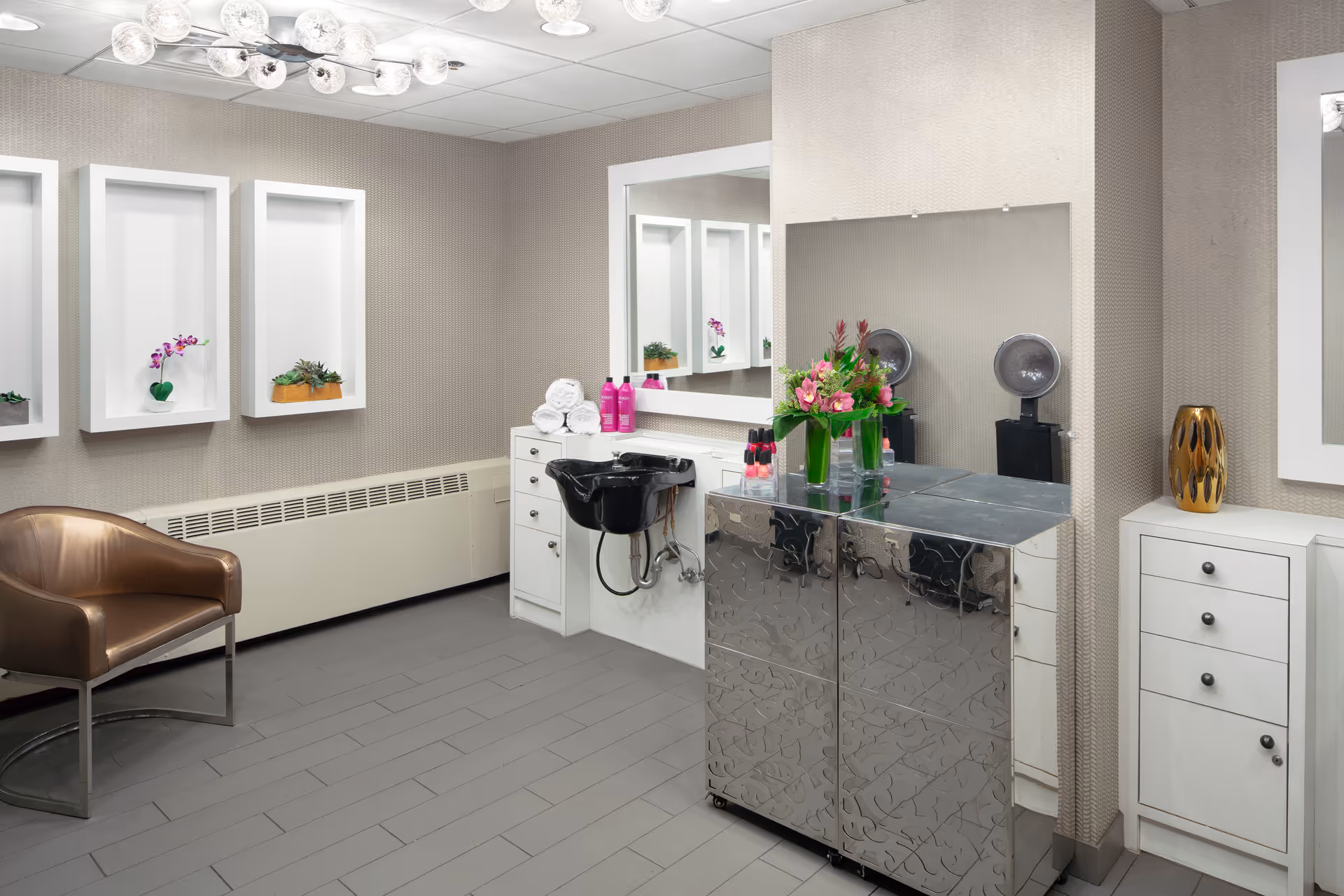 Hair salon station inside Avantara Evergreen Park senior living facility, featuring mirrors, chair, sink, and flowers.