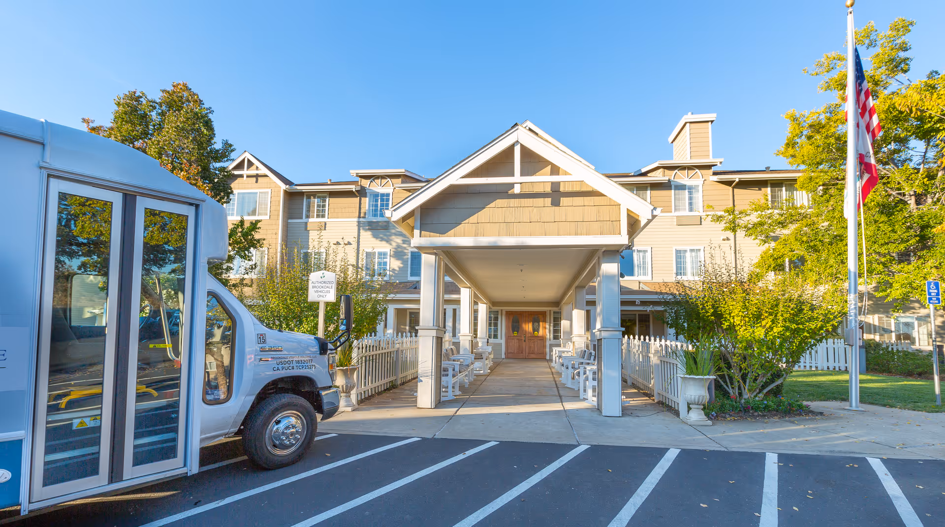 Front view of Brookdale Auburn senior living facility with covered entrance, bus, and American flag.