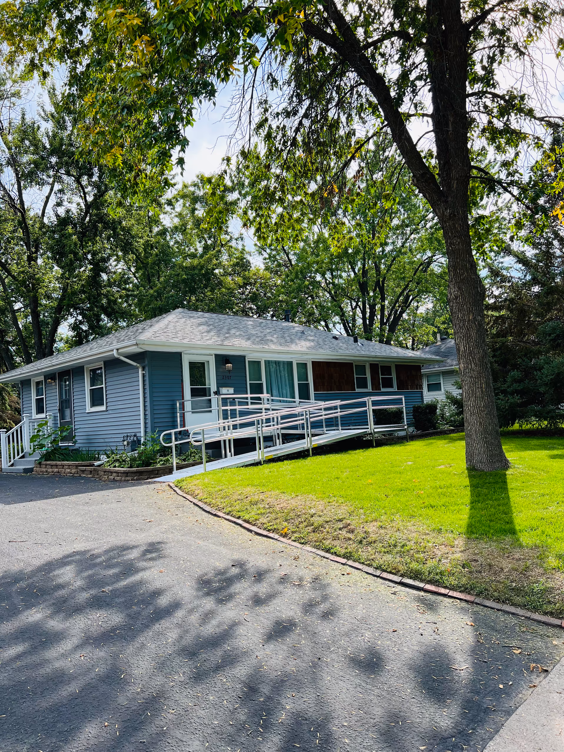 Single-story blue building with a wheelchair ramp, surrounded by green lawn and trees.