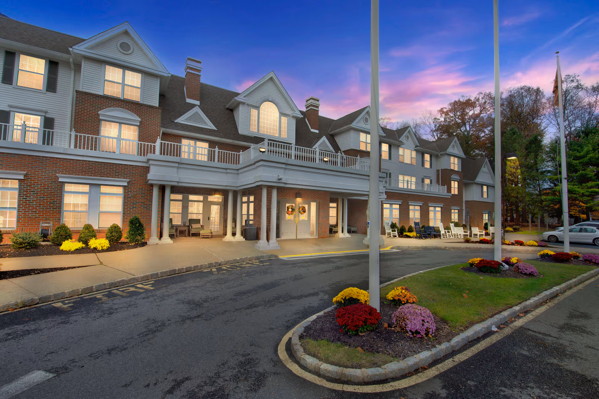 Exterior view of a brick and white senior living facility with a landscaped driveway.