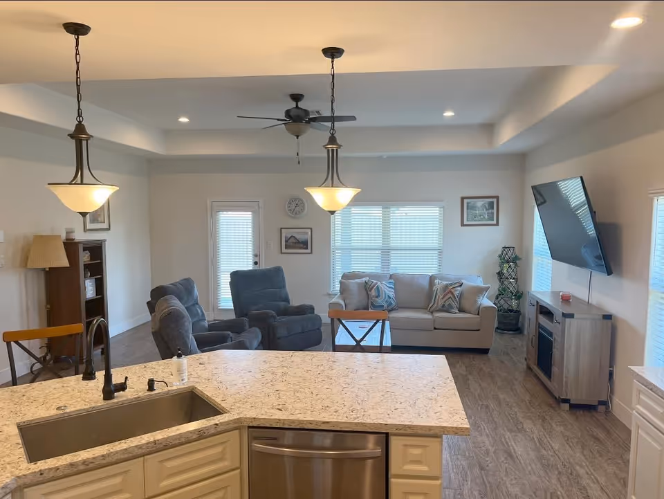 Open-concept living area with kitchen island, sofa, recliners, and wall-mounted TV.