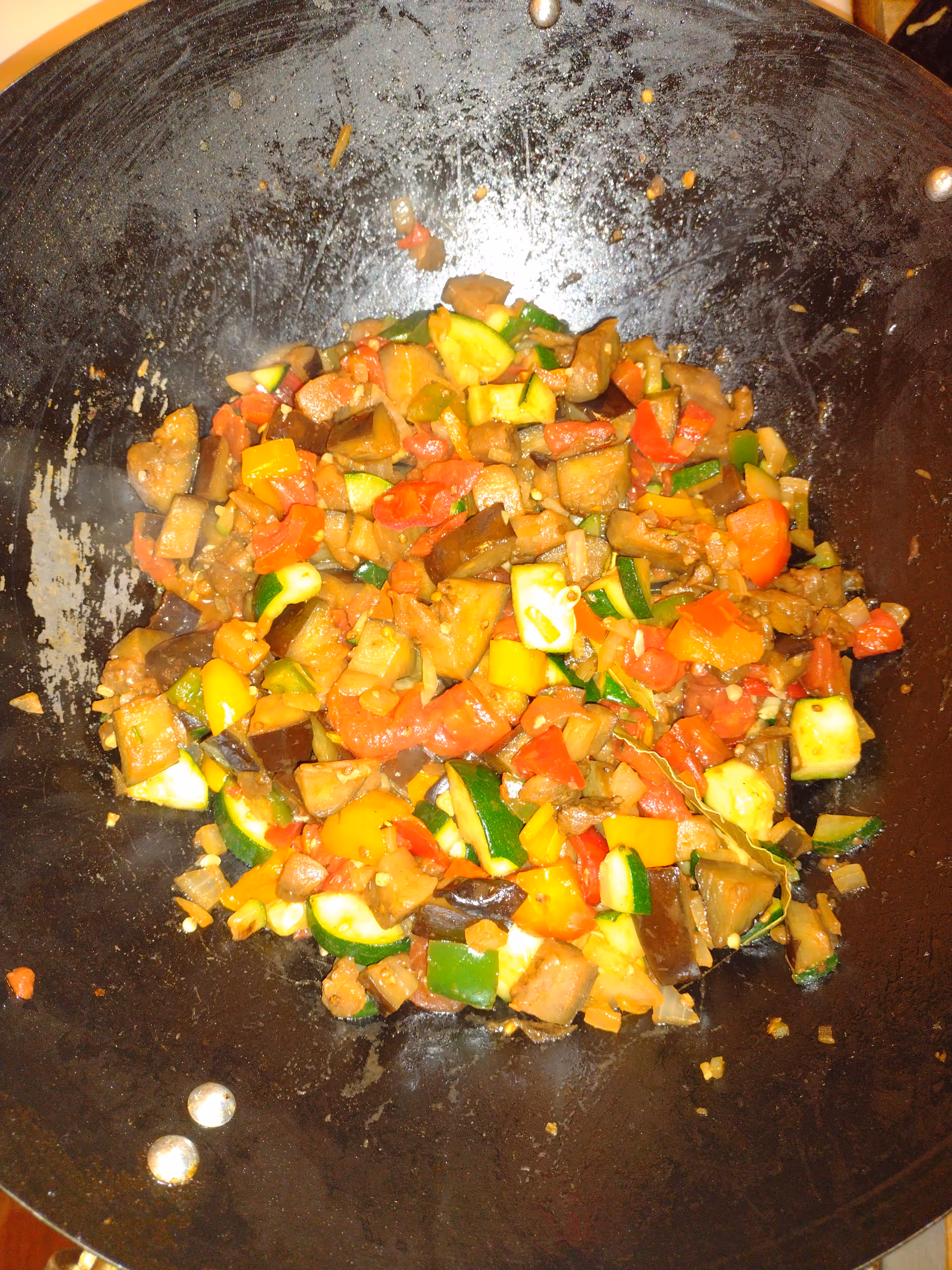 Colorful diced vegetables stir-frying in a large black wok on the stove.