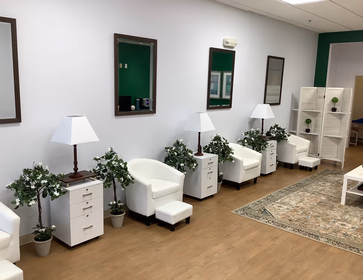 Row of white chairs, small white cabinets, and lamps along a waiting room wall.