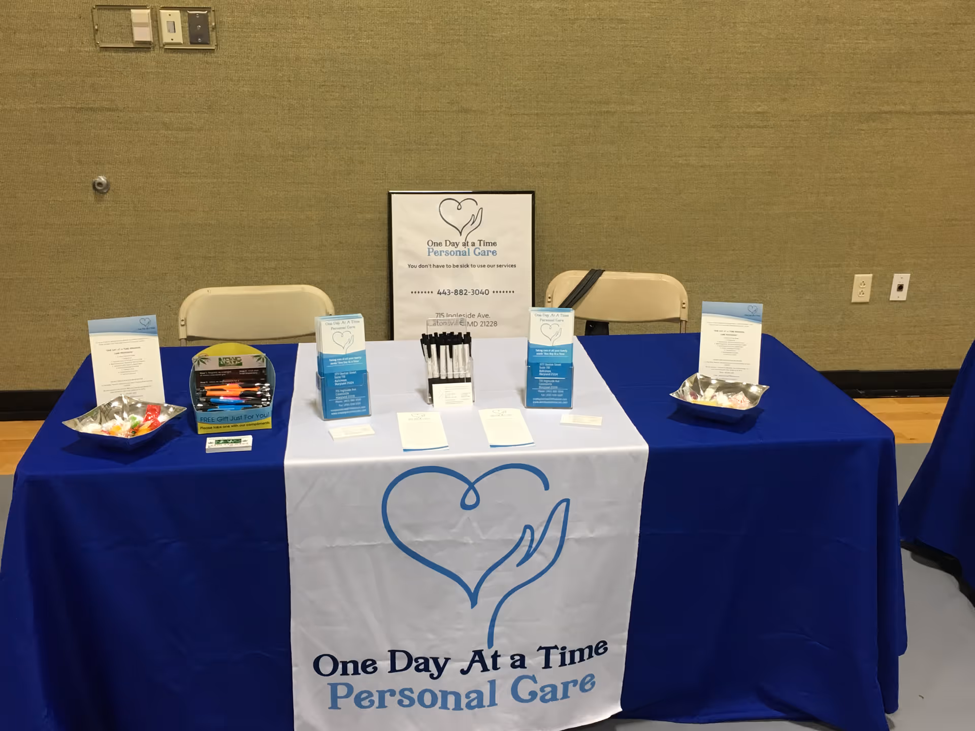Indoor information booth for One Day At A Time Personal Care with brochures on blue table.