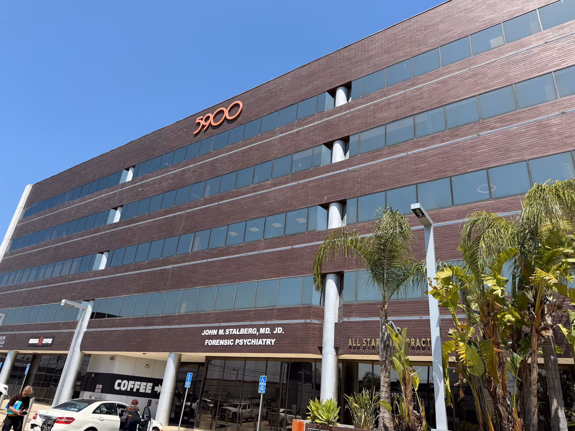 A multi-story brick office building with large windows and palm trees in front.
