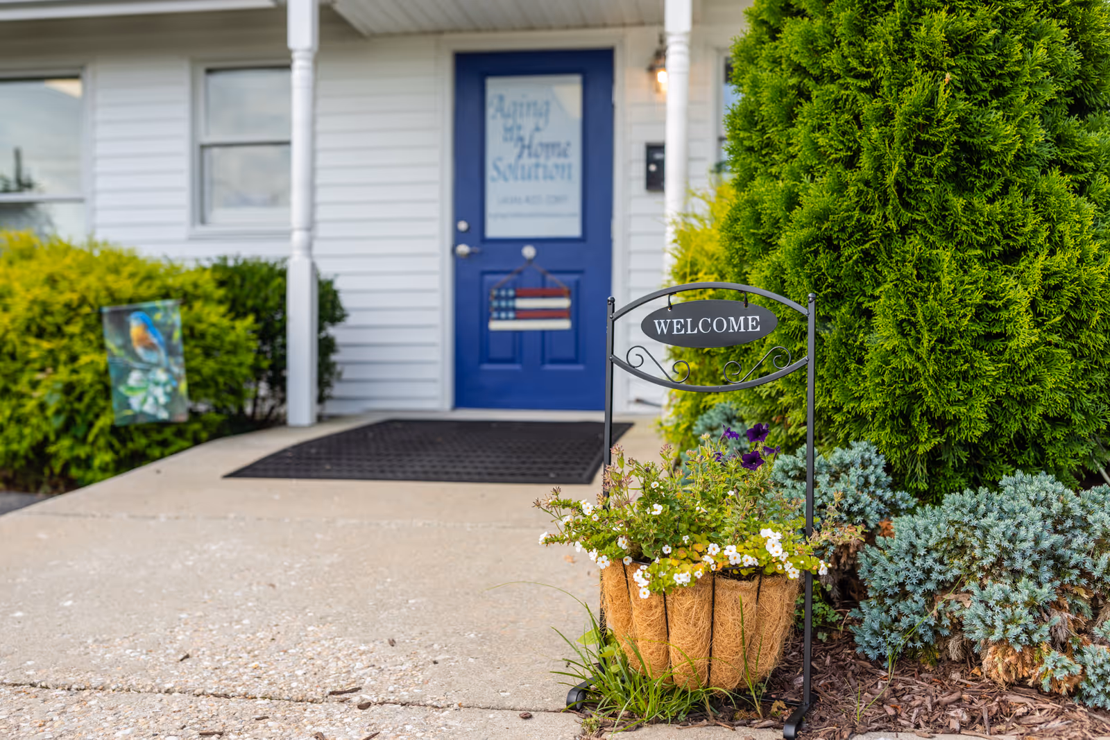 Front entrance of a senior living home with a blue door and flower planter