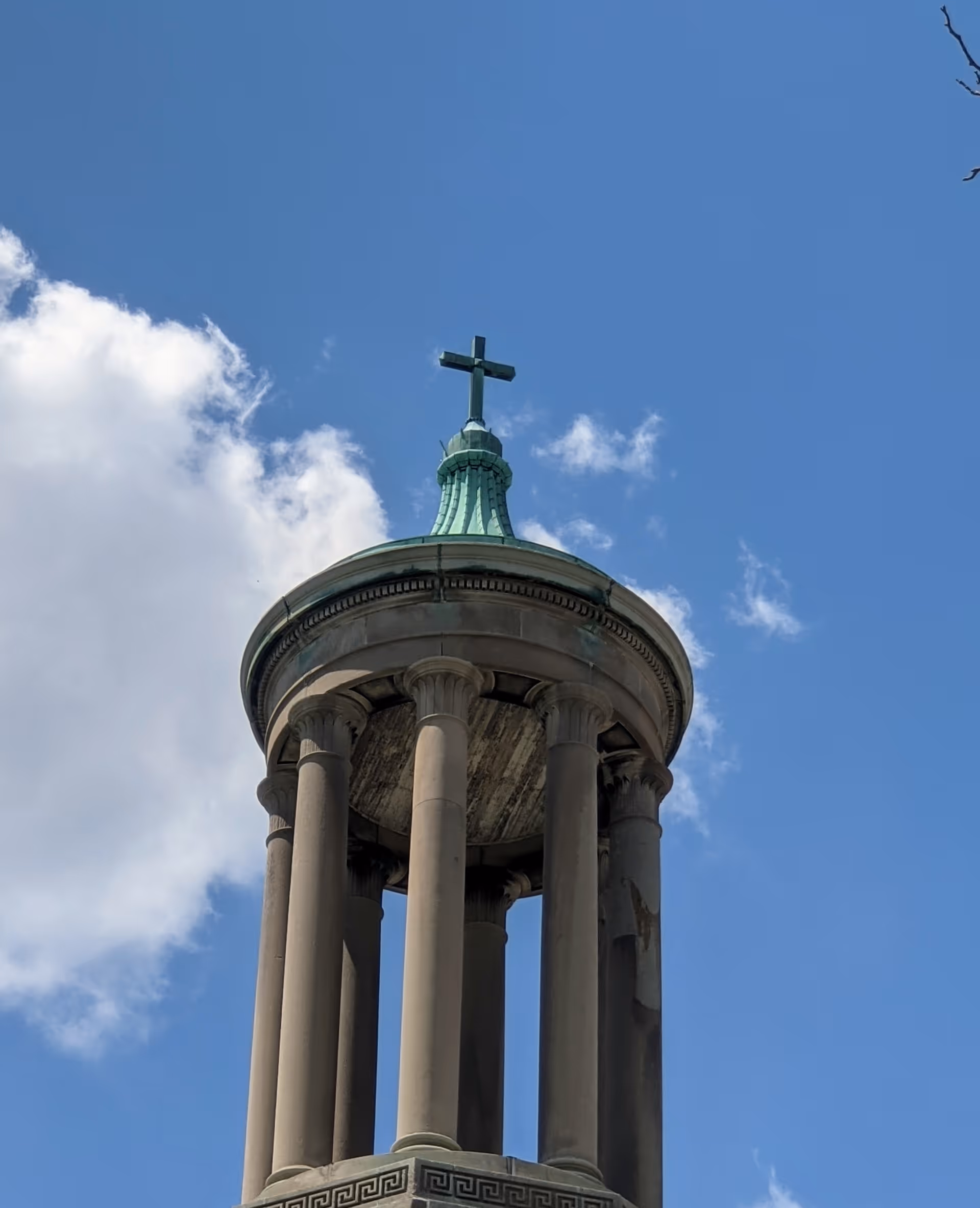 Circular colonnade tower with a green copper dome and cross against a blue sky.