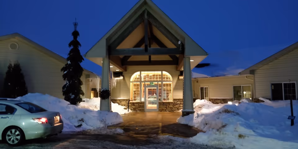 Evening view of Good Samaritan Society Albert Lea entrance with snow piled outside, car nearby.