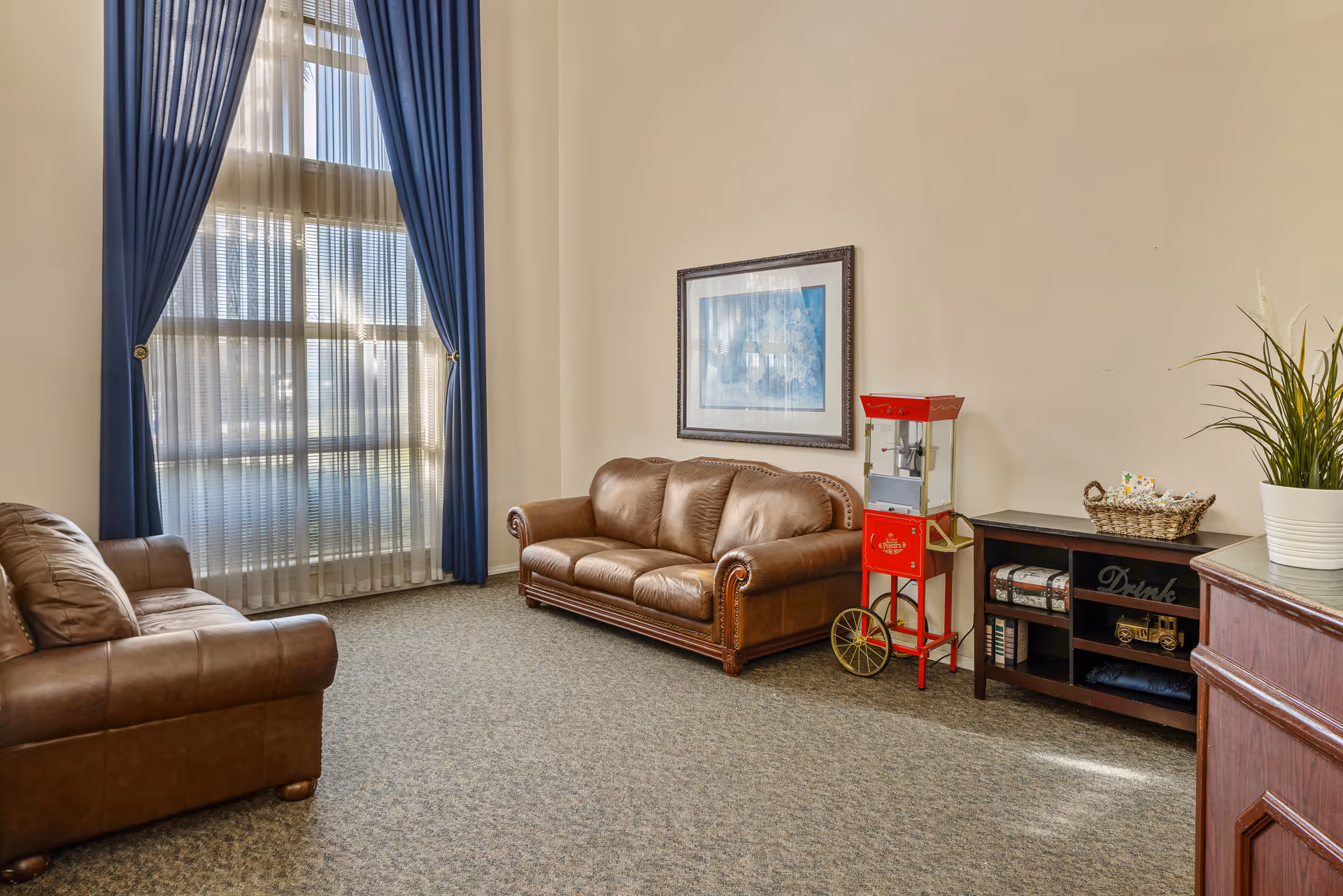 Cozy lounge area with brown leather sofas, a popcorn cart, and large windows.